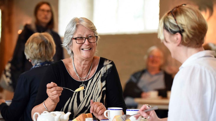 Two women sitting eating cake and drinking tea at a table in the Brewhouse Café at Knole, Kent.